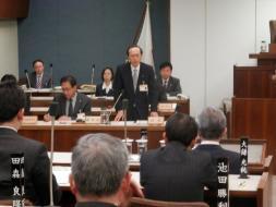 平成29年3月市議会3。皆スーツ姿で、議員達の座っている中で、市長が立って発言している写真。