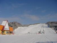 青い空の下、白い雪の積もったスキー場のゲレンデ、両脇には葉の白く雪の積もった樹木、左手に高い三角屋根のロッジが見える写真
